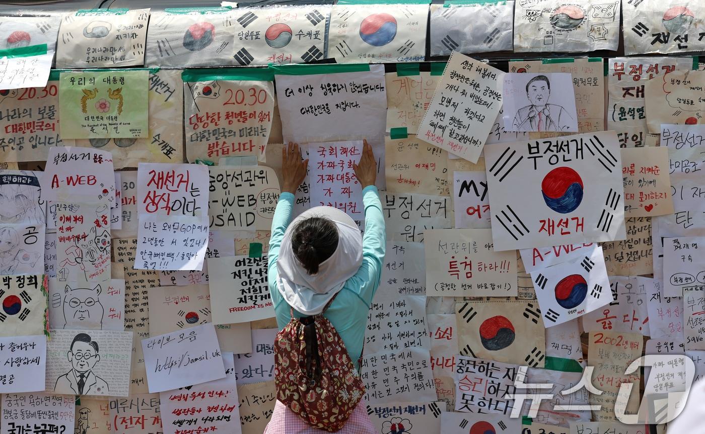 본문 이미지 - 6·3 지방선거 투표용지 부족사태로 인한 '잠실 봉쇄시위'가 25일째를 맞은 25일 서울 송파구 올림픽공원 핸드볼경기장에서 참가자가 매표소 건물에 메시지를 적은 종이를 붙이고 있다. 2026.6.29 ⓒ 뉴스1 구윤성 기자