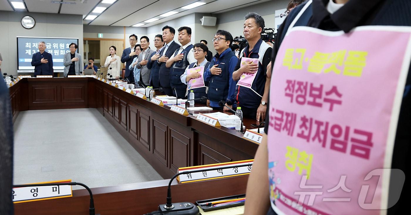 본문 이미지 - 박정훈 근로자위원이 지난 4일 세종시 정부세종청사 최저임금위원회에서 열린 2027년도 최저임금위원회 3차 전원회의에 참석하여 특고·플랫폼 적정보수 밒 도급제 최저임금 쟁취 문구를 착용한 채 국민의례를 하고 있다.ⓒ 뉴스1 김기남 기자