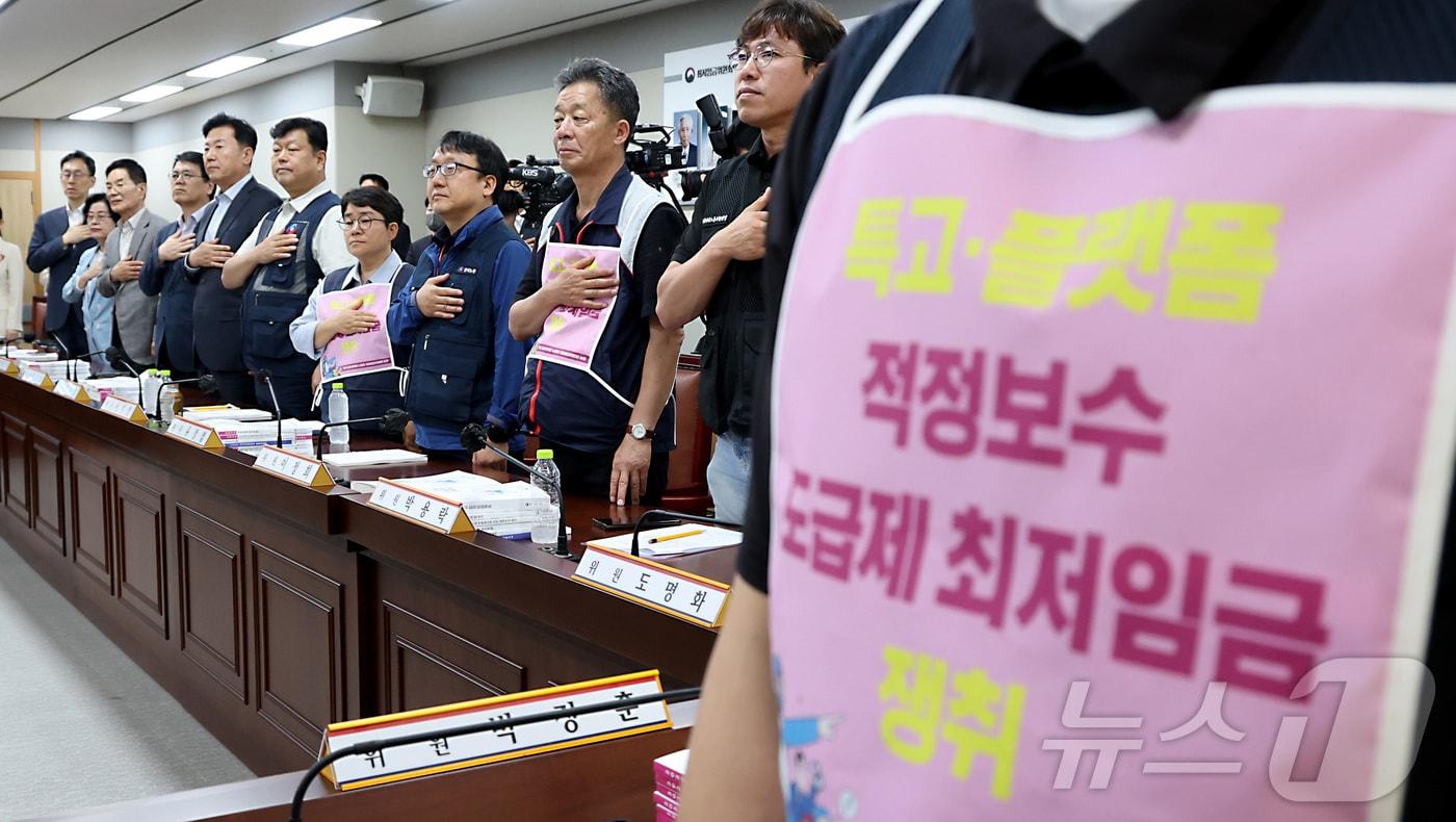 본문 이미지 - 박정훈 근로자위원이 26일 세종시 정부세종청사 최저임금위원회에서 열린 2027년도 최저임금위원회 3차 전원회의에 참석하여 특고·플랫폼 적정보수 밒 도급제 최저임금 쟁취 문구를 착용한 채 국민의례를 하고 있다. 2026.6.4 ⓒ 뉴스1 김기남 기자