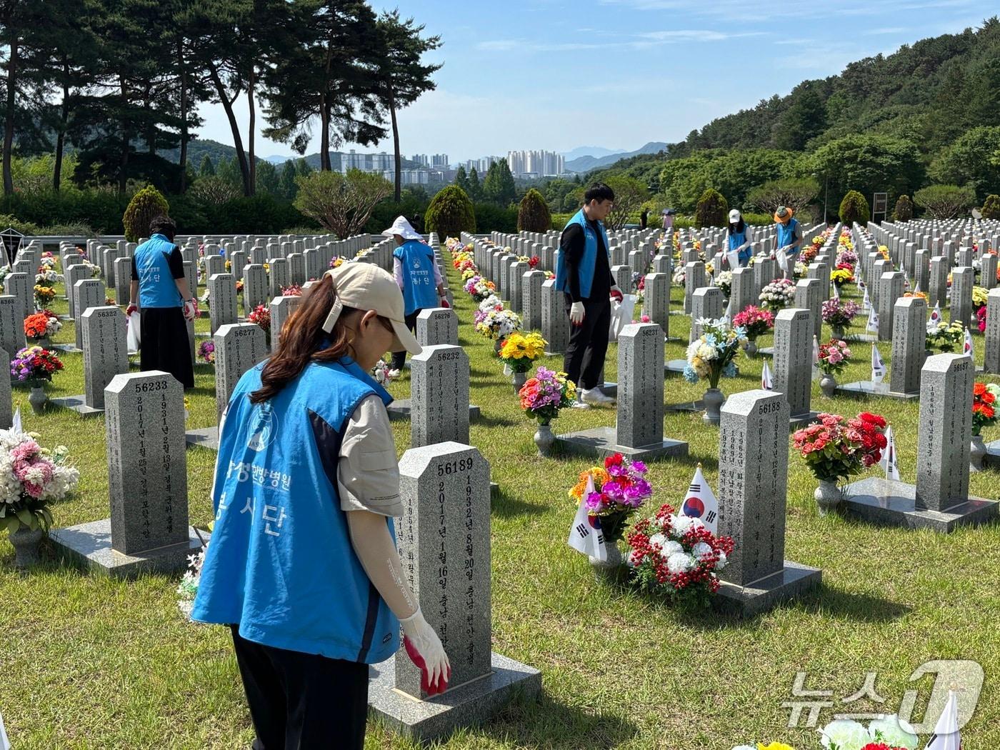 본문 이미지 - 대전자생한방병원 임직원과 대전자생봉사단원들이 국립대전현충원 묘역에서 비석을 정비하고 태극기를 꽂고 있다.(자생의료재단 제공)