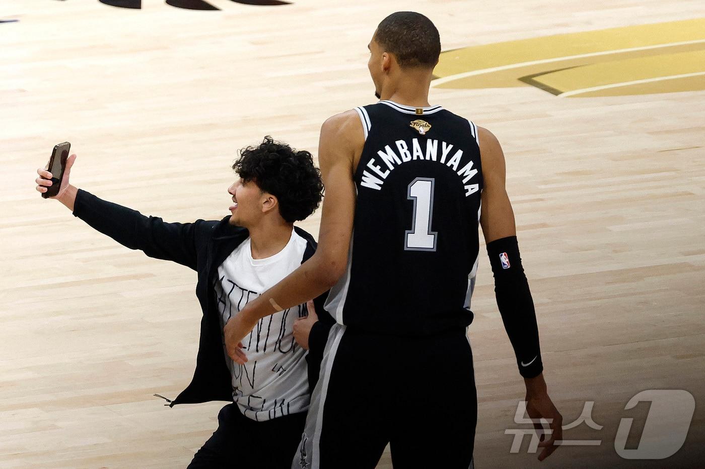 본문 이미지 - NBA 파이널 1차전 도중 코트에 난입한 팬이 웸반야마와 사진을 찍고 있다. ⓒ AFP=뉴스1