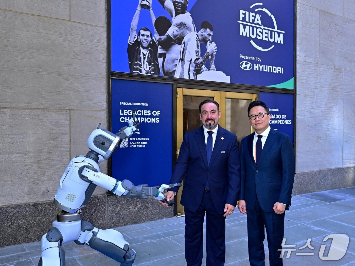 본문 이미지 - 미국 뉴욕 록펠러 센터에서 8일(현지시각) 열린 국제축구연맹(FIFA) 박물관 'FIFA 뮤지엄' 개관식에서 지성원 현대자동차 브랜드마케팅본부장 부사장(오른쪽)과 마르코 파초네 FIFA 뮤지엄 관장(왼쪽)이 휴머노이드 로봇 '아틀라스'와 함께 기념 사진을 촬영한 모습(현대차 제공). 2026.6.8.