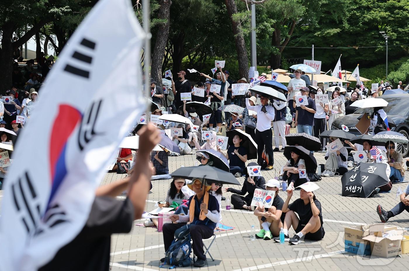 본문 이미지 - 제9회 전국동시지방선거 투표용지 부족 사태에 반발한 시민들이 9일 서울 송파구 올림픽공원 핸드볼경기장에 설치된 개표소 앞에서 재선거를 촉구하며 구호를 외치고 있다. 2026.6.9 ⓒ 뉴스1 김성진 기자