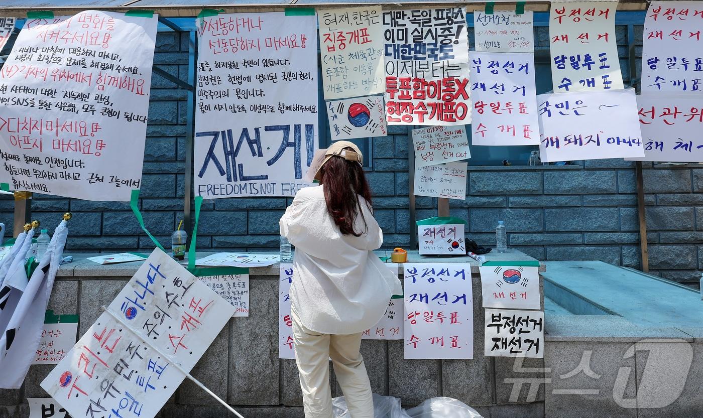 본문 이미지 - 제9회 전국동시지방선거 투표용지 부족 사태에 반발한 시민들이 9일 서울 송파구 올림픽공원 핸드볼경기장에 설치된 개표소 앞에서 재선거를 촉구하며 피켓을 붙이고 있다. 2026.6.9 ⓒ 뉴스1 김성진 기자