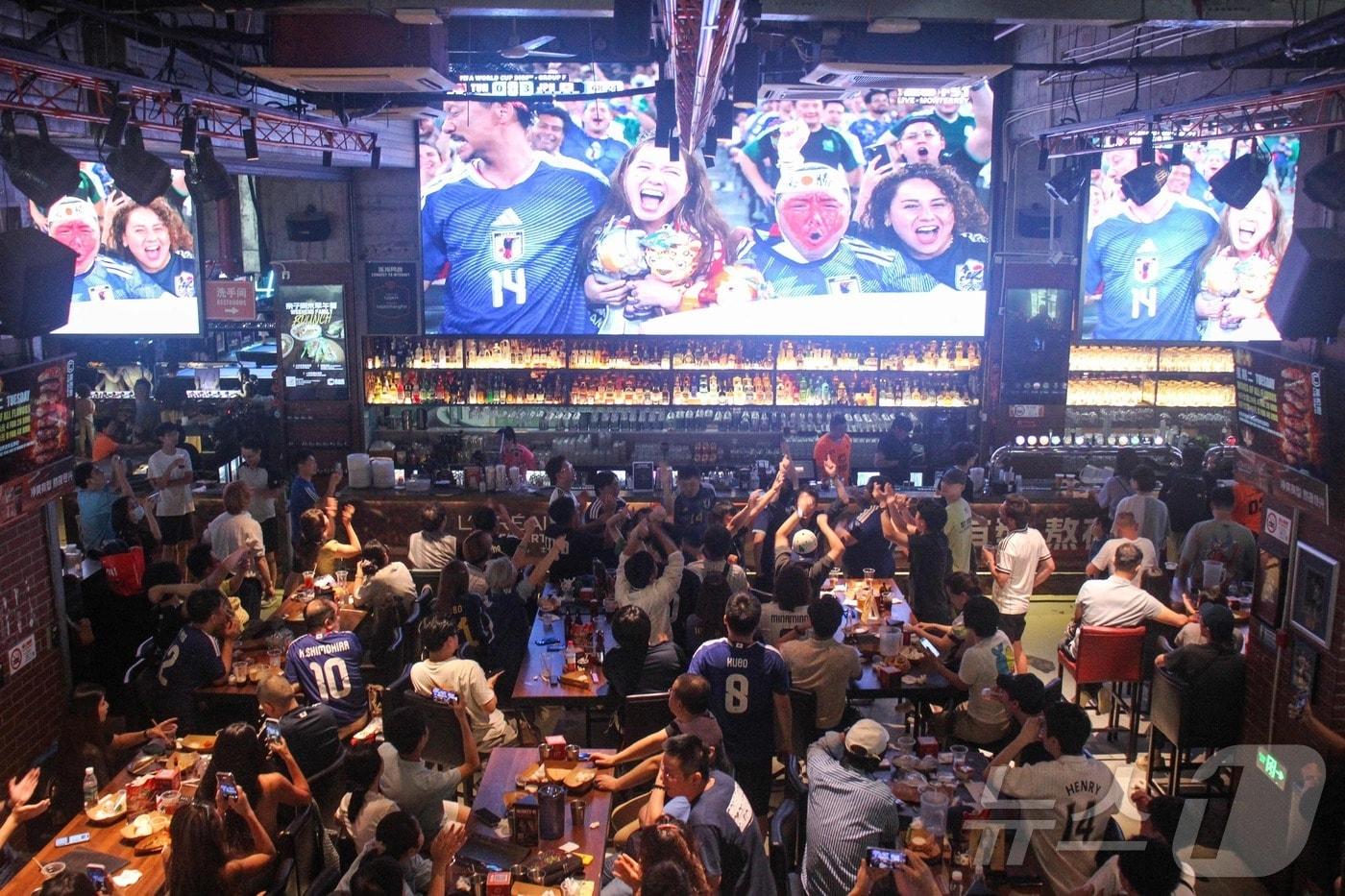 본문 이미지 - 21일 중국 상하이의 한 펍에서 중국 축구팬들이 2026 북중미 월드컵 F조 조별 예선인 일본과 튀니지 간 경기를 관람하고 있다. 일부 팬들은 일본 축구대표팀의 유니폼을 입고 일본 선수를 응원하기도 했다. 2026.6.21 ⓒ AFP=뉴스1