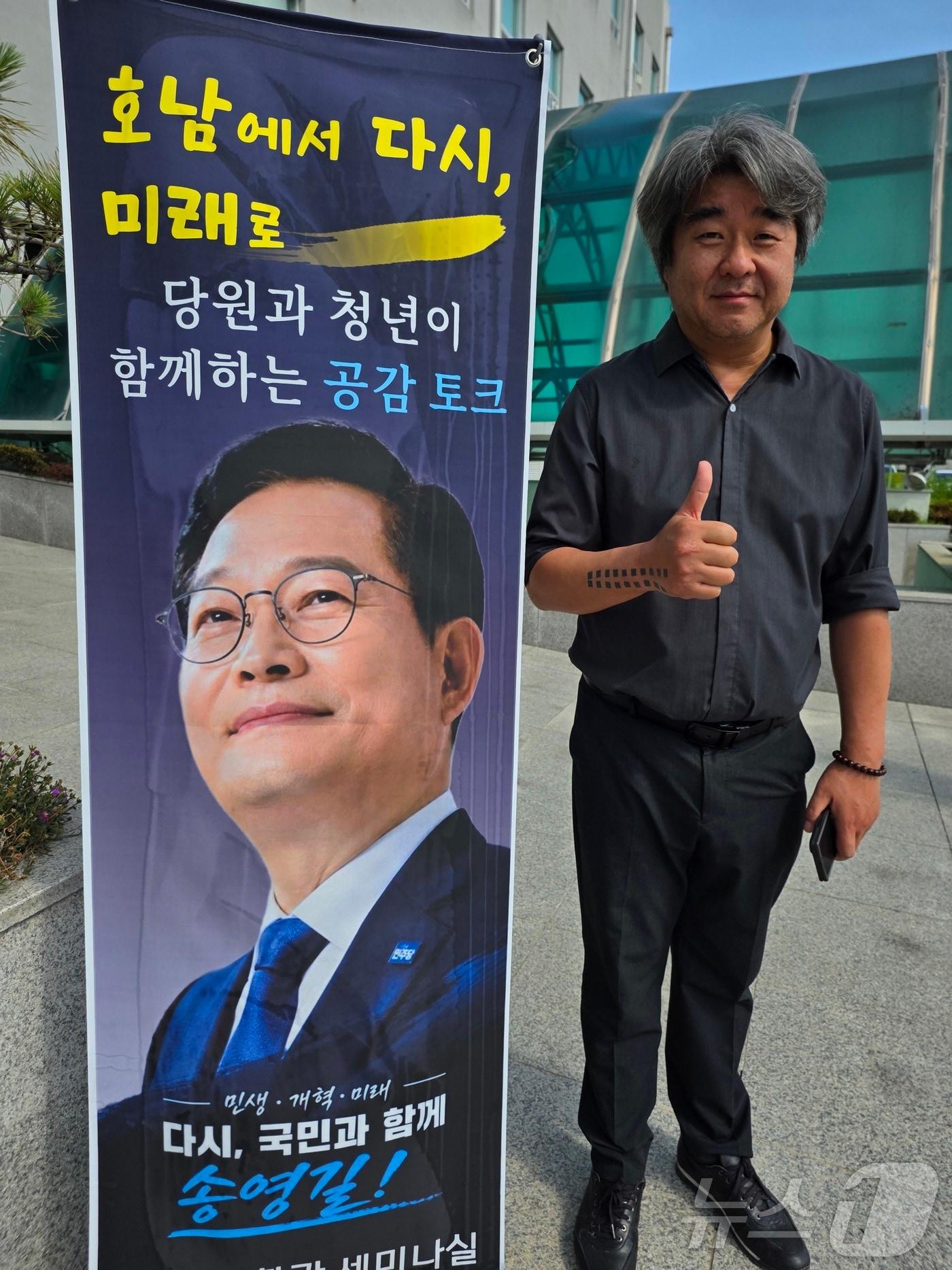 본문 이미지 - 송영길 국회의원의 수행실장인 김진석 전 청와대 전속 사진 담당 행정관이 10일 광주 서구 염주체육관에서 송 의원 플래카드 옆에 섰다.  2026.7.10 ⓒ 뉴스1 서충섭 기자