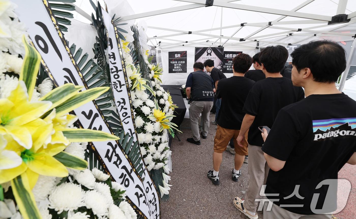 본문 이미지 - 14일 경기 수원시 영통구 삼성전자 수원사업장 중앙문에서 열린 'DX부문 사기진작 및 보상마련 촉구 집회'에서 조합원들이 '2026 DX부문 사망선고 위로를 위한 조문 행사'에 참여하고 있다. 2026.7.14 ⓒ 뉴스1 김영운 기자