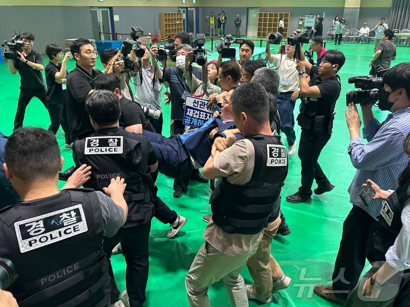 본문 이미지 - 맹정섭 민주당 충주시장 후보가 15일 충주시장선거 재검표가 진행되는 교통대 체육관에서 CCTV파일과 투표지 이미지 스캔 파일을 공개하라고 요구하다 선관위 제지에 퇴장 당하고 있다. 2026.7.15 ⓒ 뉴스1 윤원진 기자