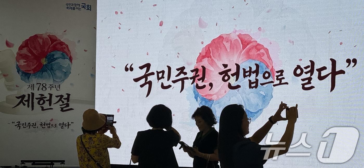 본문 이미지 - 제78주년 제헌절을 하루 앞둔 16일 서울 여의도 국회를 찾은 참관객들이 로텐더홀에 마련중인 경축식 행사장을 배경으로 기념 촬영을 하고 있다. 2026.7.16 ⓒ 뉴스1 유승관 기자