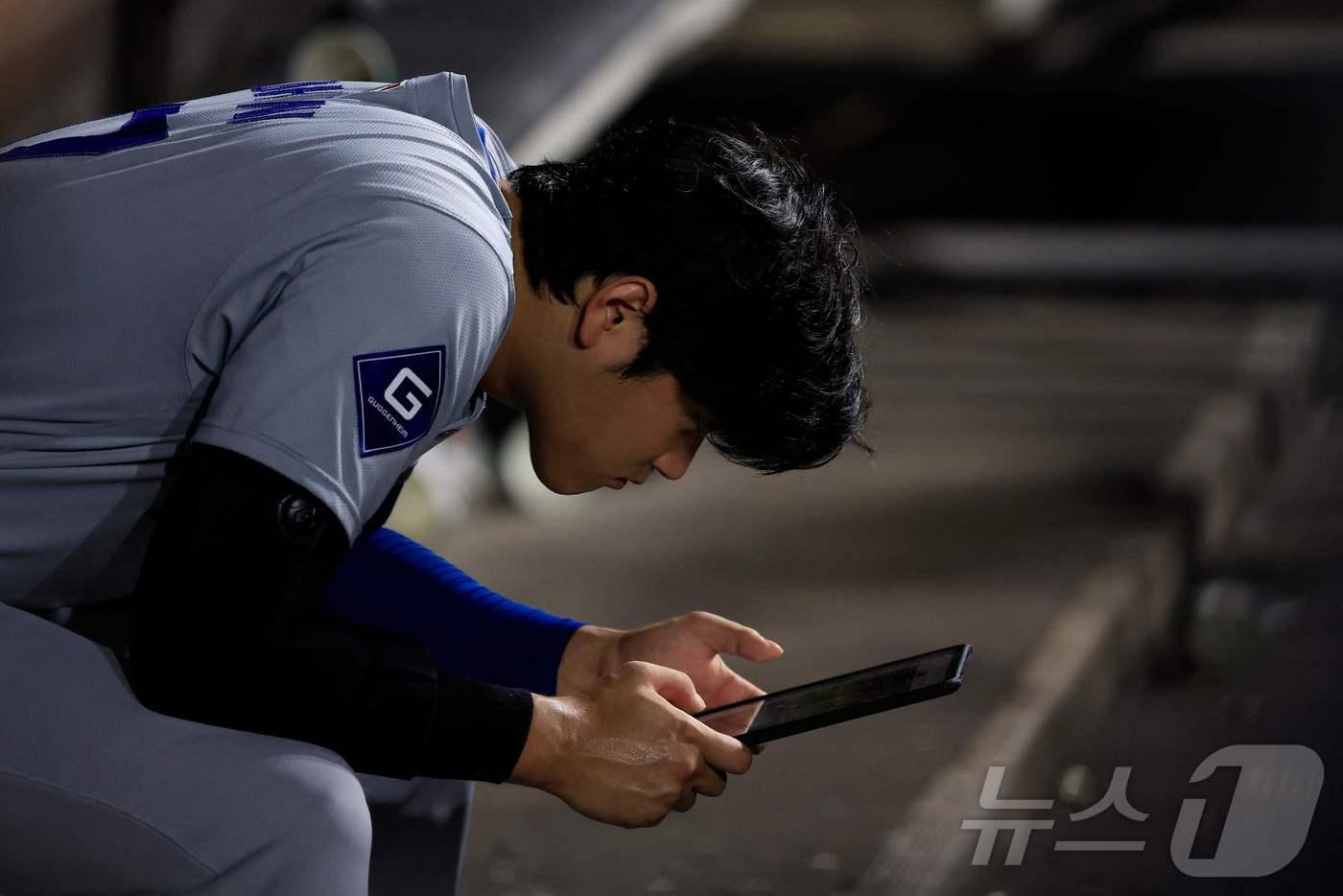 본문 이미지 - 더그아웃에서 태블릿 PC를 보고 있는 오타니. ⓒ AFP=뉴스1