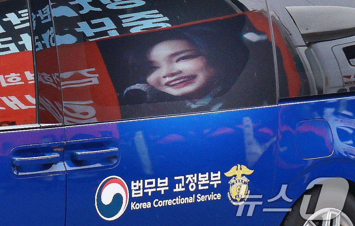 본문 이미지 - 김건희 여사를 태운 호송차가 22일 경기 과천 2차 종합특검 사무실 지하주차장으로 들어서고 있다. 김여사가 탄 차량에 지지자들이 마련한 김 여사 사진이 비춰지고 있다. 2차 종합특검팀(특별검사 권창영)은 이날 윤석열 전 대통령 관저 이전과 관련 특정범죄가중처벌법상 알선수재와 직권남용 혐의로 김 여사를 피의자 신분으로 소환했다. 2026.7.22 ⓒ 뉴스1 이호윤 기자