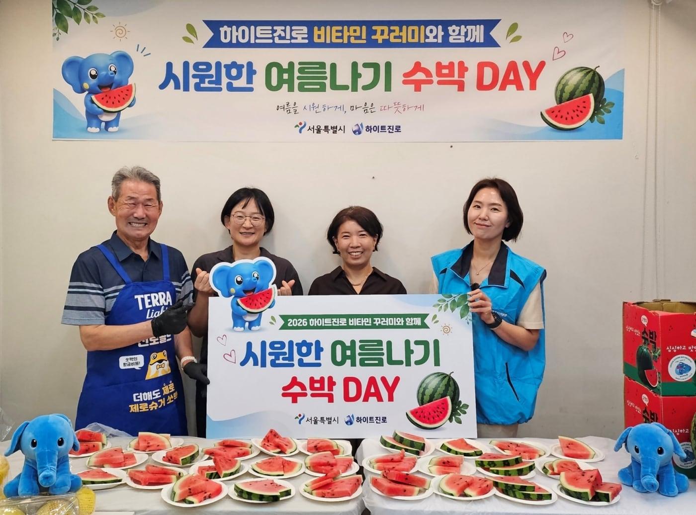 본문 이미지 - 서울역 쪽방촌에서 2026 하이트진로 비타민 꾸러미와 함께 시원한 여름나기 ‘수박 DAY' 행사가 열렸다. (왼쪽부터) 쪽방촌 주민, 이신옥 서울시 팀장, 유호연 서울역 쪽방상담소 소장, 하이트진로 관계자가 기념 촬영을 하고 있다.(하이트진로 제공)