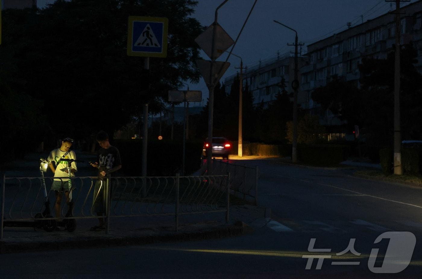 본문 이미지 - 6월 30일(현지시간) 러시아가 점령한 크림반도 휴양 도시 예프파토리야에서 청소년들이 정전으로 어두워진 거리에 서 있다. 2026.06.30. ⓒ 로이터=뉴스1