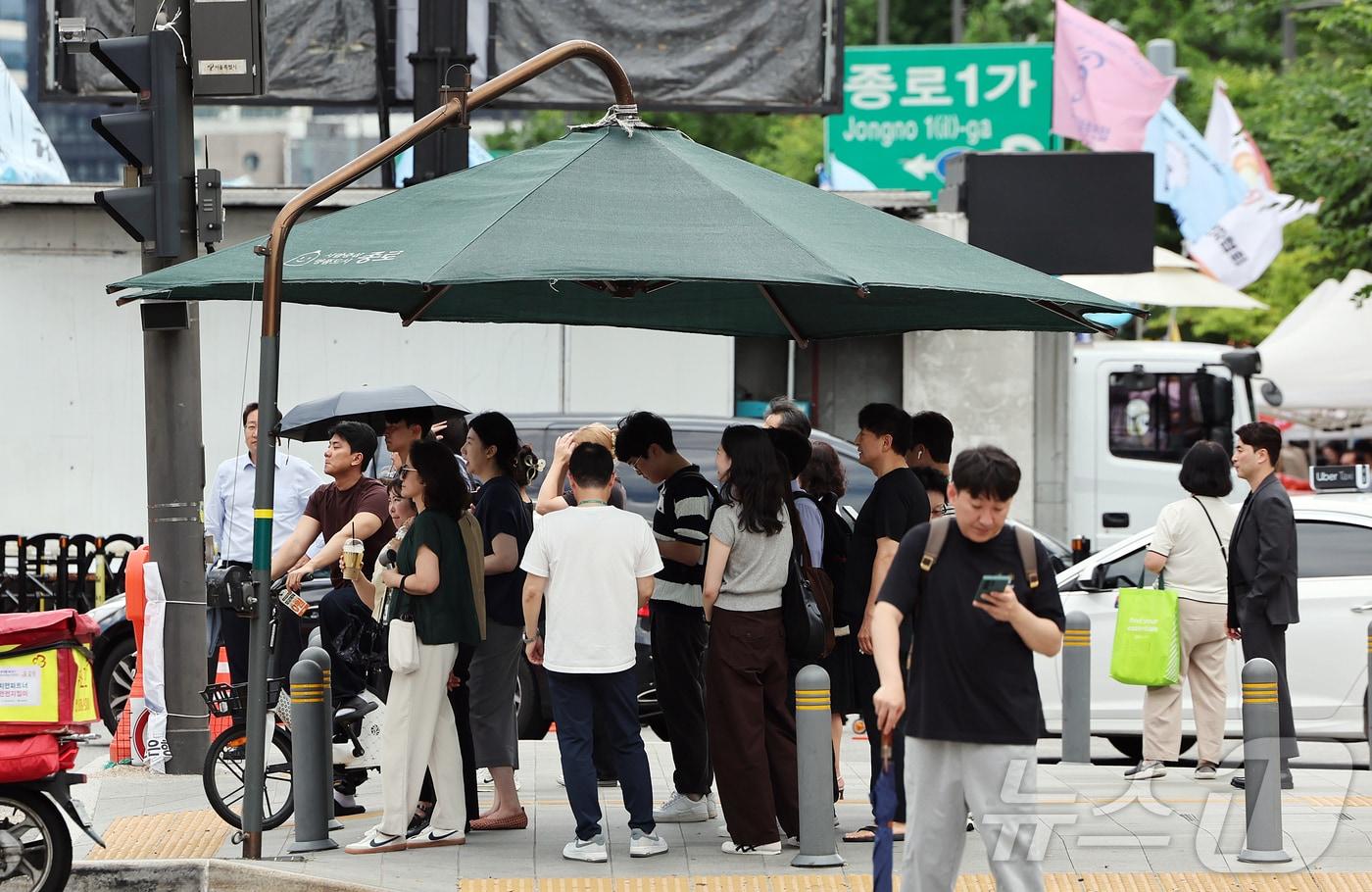 본문 이미지 - 절기상 본격적인 더위가 시작된다는 소서(小暑)이자 무더운 날씨를 보인 7일 오후 서울 종로구 광화문사거리에 설치된 대형 그늘막에서 시민들이 신호를 기다리며 햇빛을 피하고 있다. 2026.7.7 ⓒ 뉴스1 김진환 기자