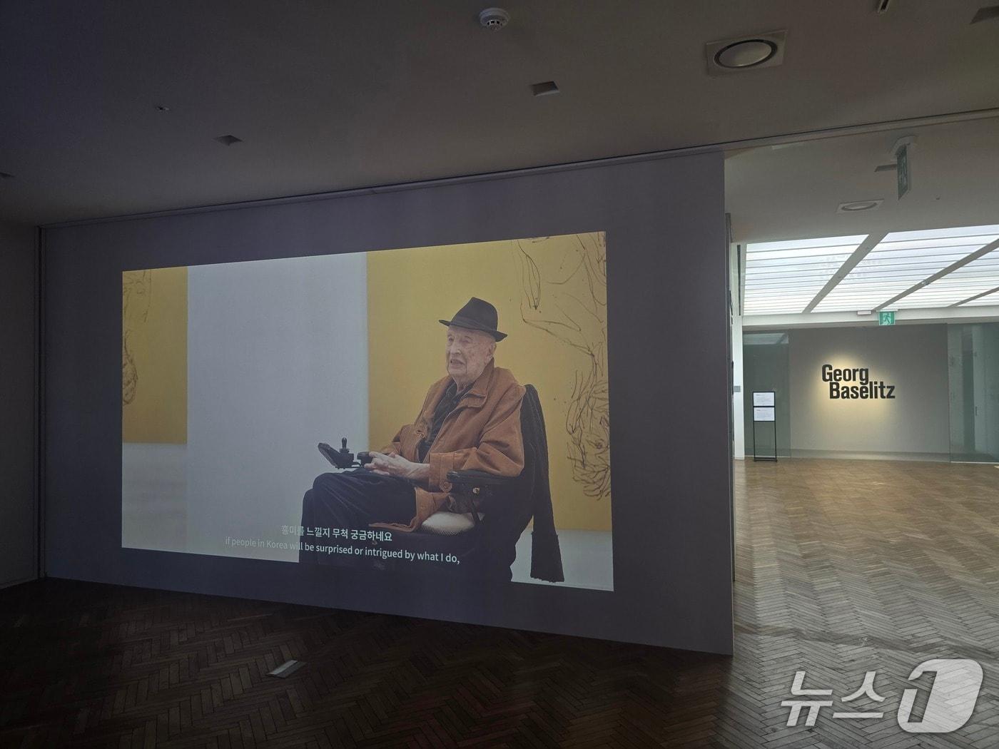본문 이미지 - '게오르그 바젤리츠 회고전' 전시 전경. 한국 전시를 앞두고 4월 타계한 게오르그 바젤리츠가 생전 영상을 통해 한국 관람객들에게 메시지를 전하고 있다. 2026.08.12. ⓒ 뉴스1 김정한 기자