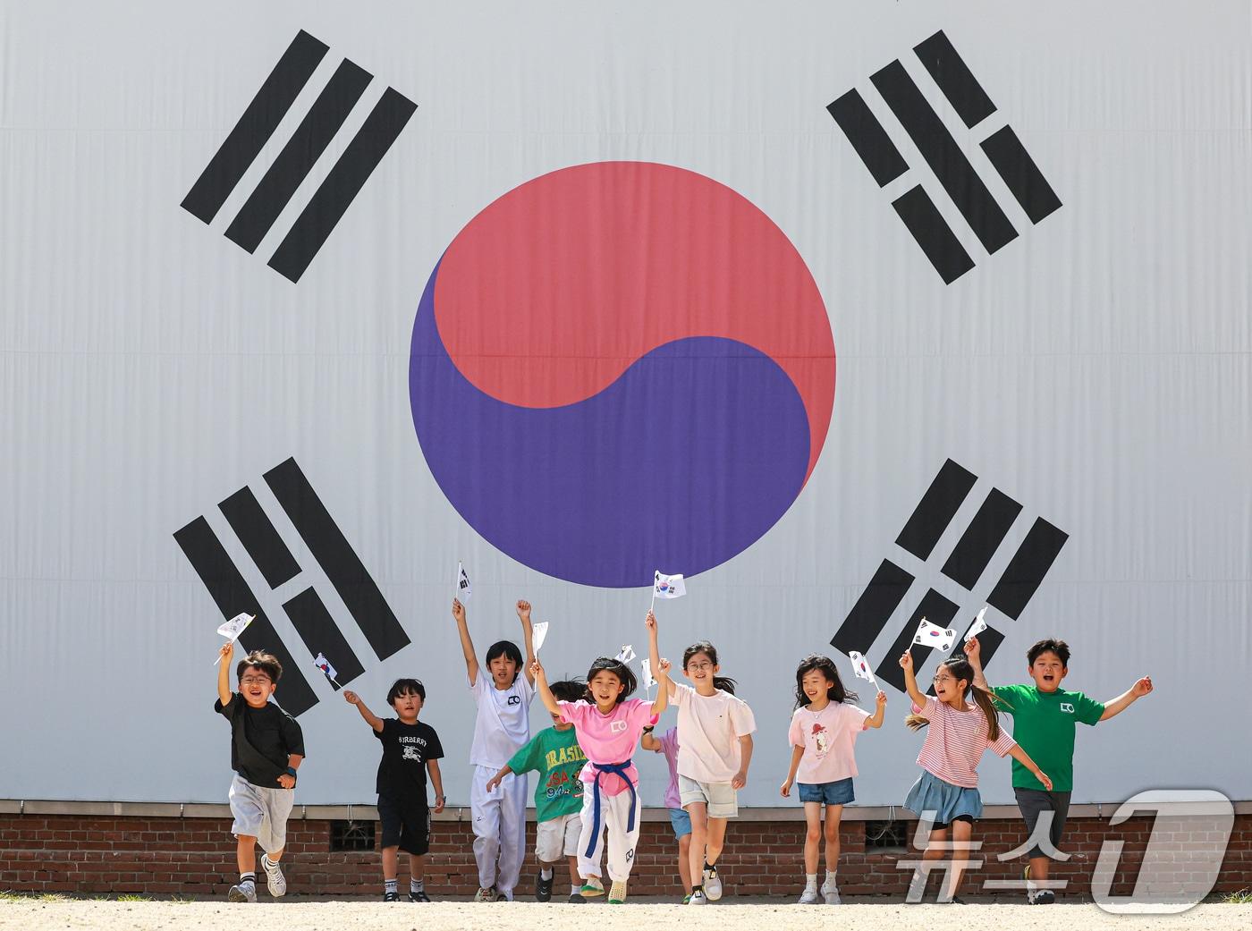 본문 이미지 - 제81주년 광복절을 하루 앞둔 14일 서울 서대문구 서대문형무소역사관 대형 태극기 앞에서 어린이들이 직접 만든 태극기를 흔들며 힘차게 뛰고 있다. 2026.8.14 ⓒ 뉴스1 이호윤 기자