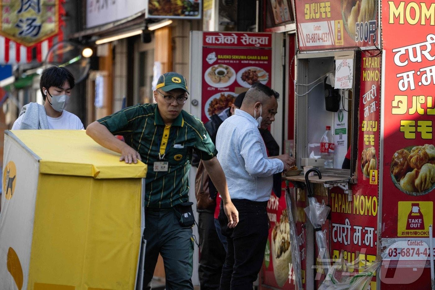 본문 이미지 - 외국인 인구가 밀집해 있는 일본 도쿄 신오쿠보 지역에서 한 남성이 네팔 식당 앞을 지나가는 모습. 2026.06.12 ⓒ AFP=뉴스1