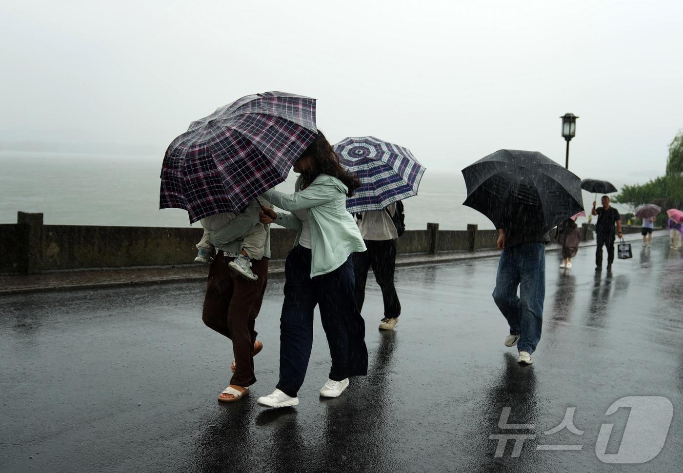 본문 이미지 - 9일 중국 동부 저장성 항저우의 서호 풍경구 단교(두안차오)에서 관광객들이 빗속을 걷고 있다. 제13호 태풍 '돌핀'이 접근함에 따라 중국 중앙기상대는 일요일 태풍 경보 체계 중 가장 높은 단계인 적색경보를 발령했다. 2026.08.09. ⓒ 신화=뉴스1