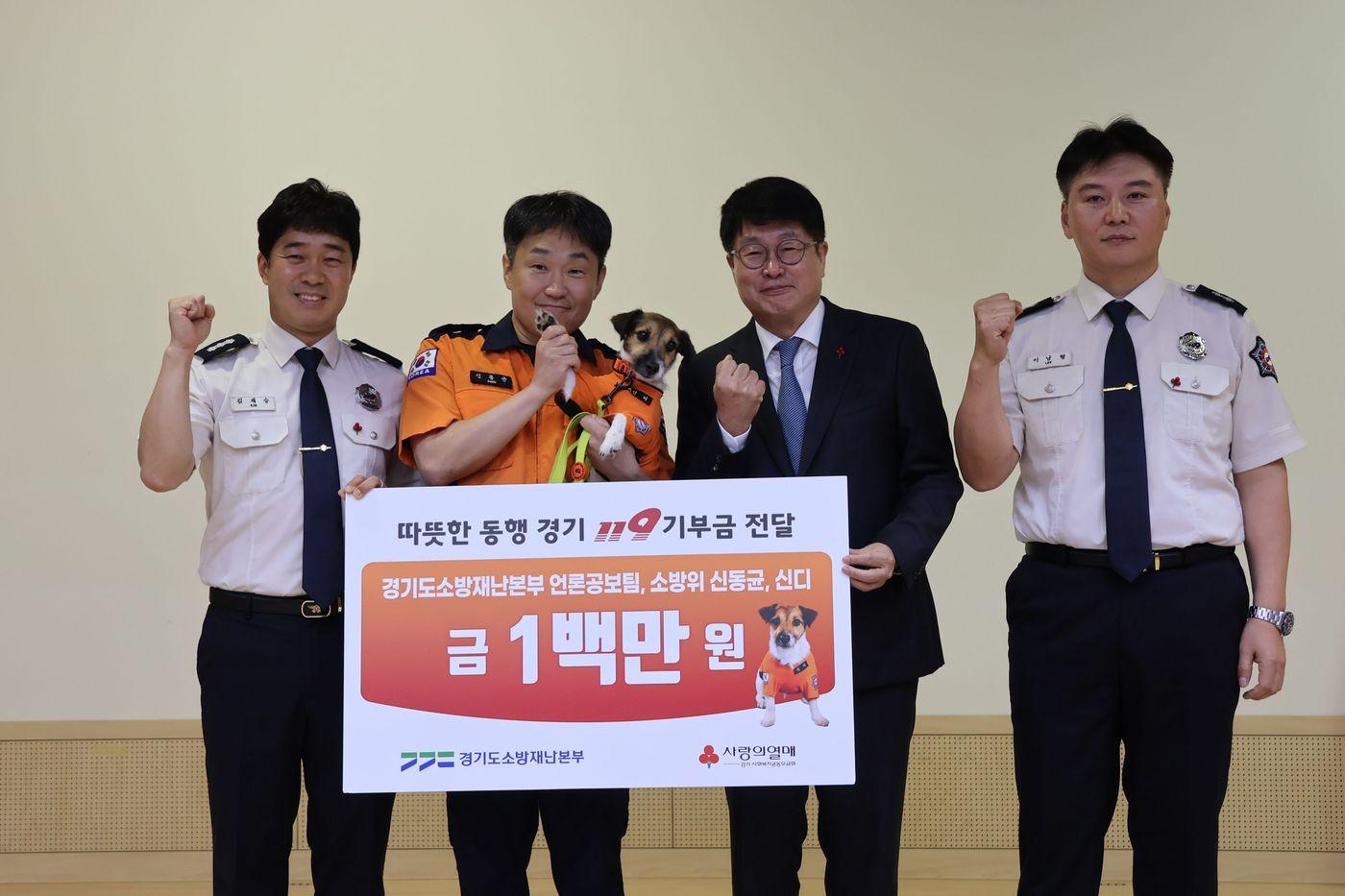 본문 이미지 - (왼쪽 두 번째부터) 신동균 소방위와 반려견 신디, 권인욱 경기 사랑의열매 회장과 경기도소방재난본부 언론공보팀 직원들이 기부금 전달 후 기념 촬영을 하고 있다.(사랑의열매 사회복지공동모금회 제공)