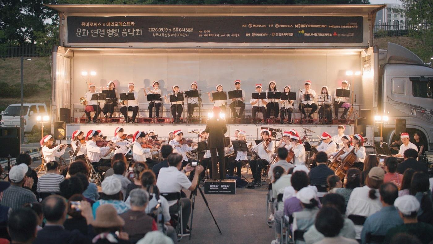 본문 이미지 - 용마로지스는 19일 경기도 김포시 마송LH4단지 아파트 주차장에서 '문화연결 별빛 음악회'를 개최했다. 이동식 무대가 된 물류트럭에서 메리 오케스트라단이 지역주민들에게 아름다운 선율을 선보이고 있다. (용마로지스 제공)