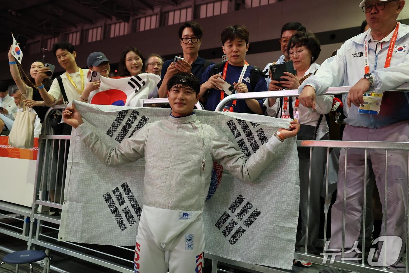 본문 이미지 - 대한민국 오상욱이 23일 일본 도코나메시 아이치 스카이 엑스포홀에서 열린 2026 아이치·나고야 아시안게임 펜싱 남자 사브르 결승에서 중국 션천평을 꺾고 금메달을 확정지은 뒤 태극기를 두르고 있다. 2026.9.23 ⓒ 뉴스1 김도우 기자