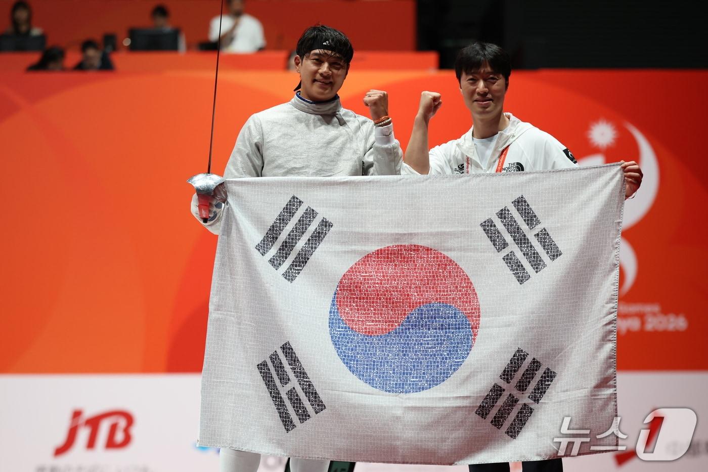 본문 이미지 - 대한민국 오상욱이 23일 일본 도코나메시 아이치 스카이 엑스포홀에서 열린 2026 아이치·나고야 아시안게임 펜싱 남자 사브르 결승에서 중국 션천평을 꺾고 금메달을 확정지은 뒤 태극기를 펼치며 환호하고 있다. 2026.9.23 ⓒ 뉴스1 김도우 기자
