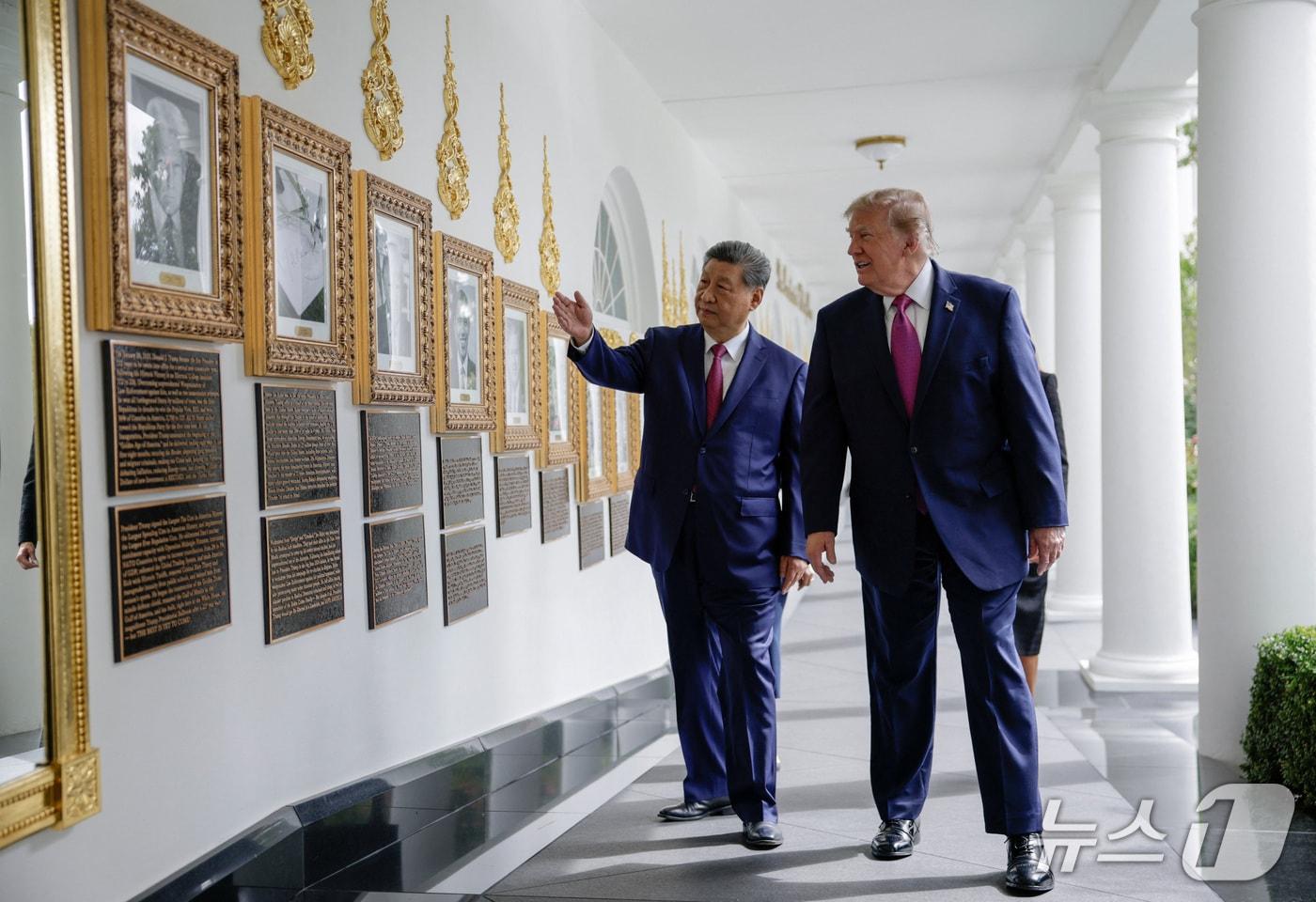 본문 이미지 - 24일 백악관 회랑에 있는 '대통령 명예의 거리'에서 도널드 트럼프 미국 대통령과 시진핑 중국 국가주석이 자동 서명기(오토펜)가 조 바이든 전 미국 대통령의 서명을 받는 사진을 보고 있다. 2026.9.24 ⓒ 로이터=뉴스1