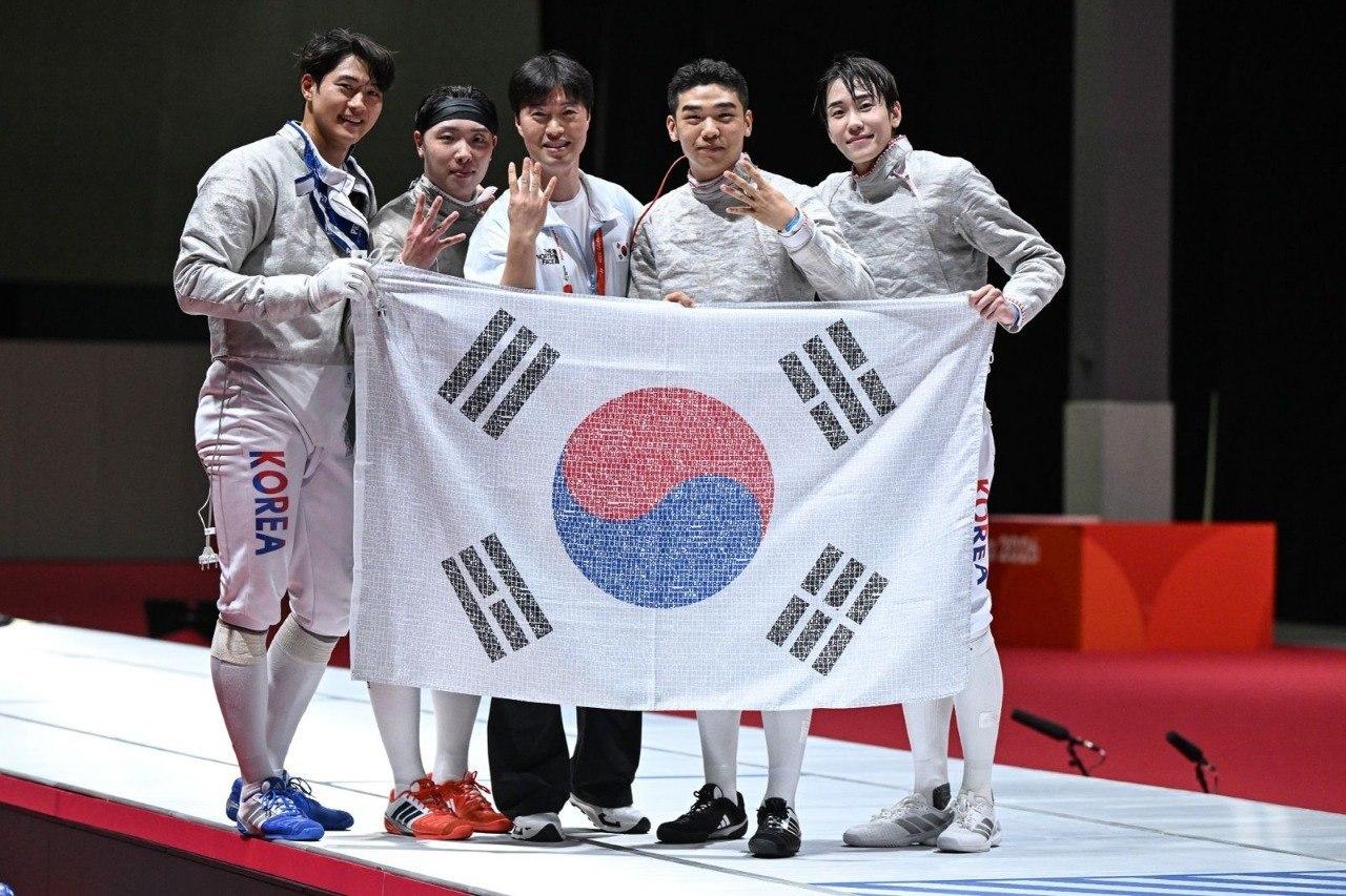 본문 이미지 - 2026 아이치·나고야 아시안게임 펜싱 남자 사브르 단체전에서 4연패를 달성한 대한민국 대표팀 선수단이 국민 응원 메시지가 담긴 태극기를 들고 기념 촬영을 하고 있다.(SK텔레콤 제공)
