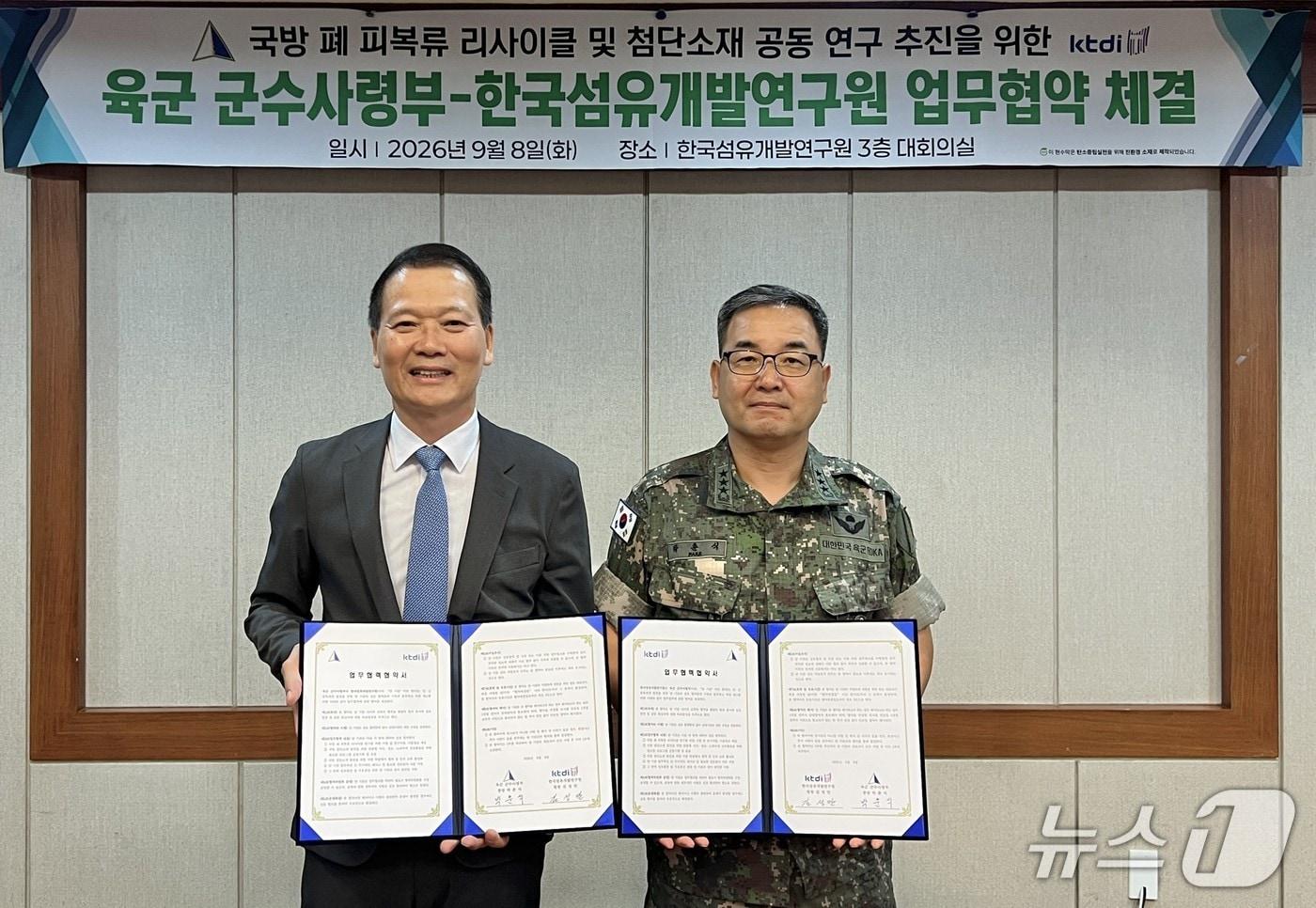 본문 이미지 - 김성만 한국섬유개발연구원장(왼쪽)과 박춘식 육군 군수사령관이 '국방 폐 피복류 리사이클 및 첨단소재 공동 연구 추진'을 위한 업무협약을 체결한 뒤 협약서를 펼쳐 보이고 있다.