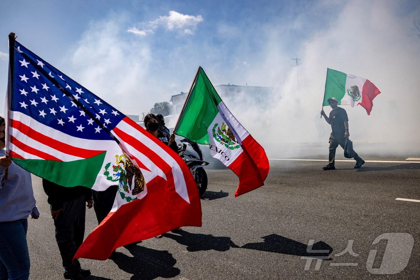 이민세관단속국(ICE)이 미국 캘리포니아주 로스앤젤레스 카운티의 파라마운트에서 불법 체류자들을 체포한 후 경찰과 시위대 간 대치 중 한 남성이 미국 성조기와 멕시코 국기를 들고 있다. 2025.6.7./뉴스1 ⓒ 로이터=뉴스1 ⓒ News1 이창규 기자 <자료사진>